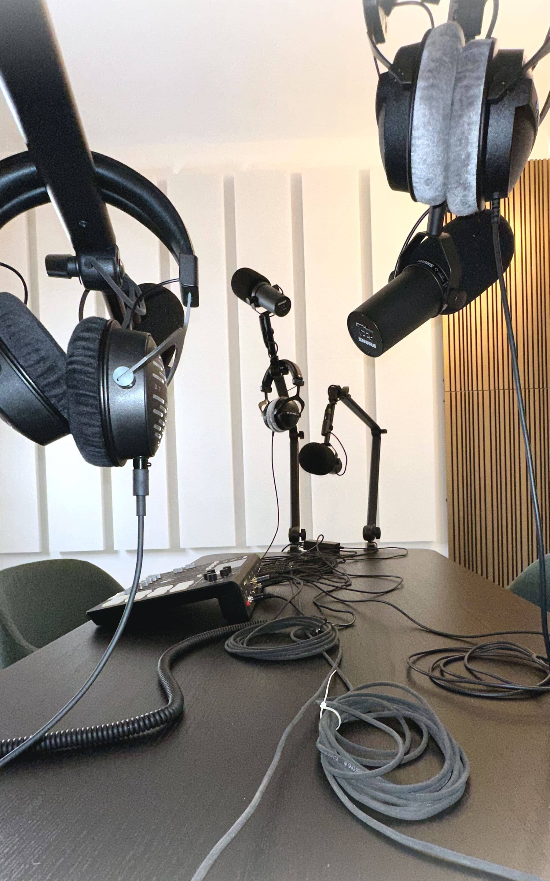 Zwei Kopfhörer hängen über dem Podcast-Tisch, dahinter Mikrofone und aufgerollte Kabel.