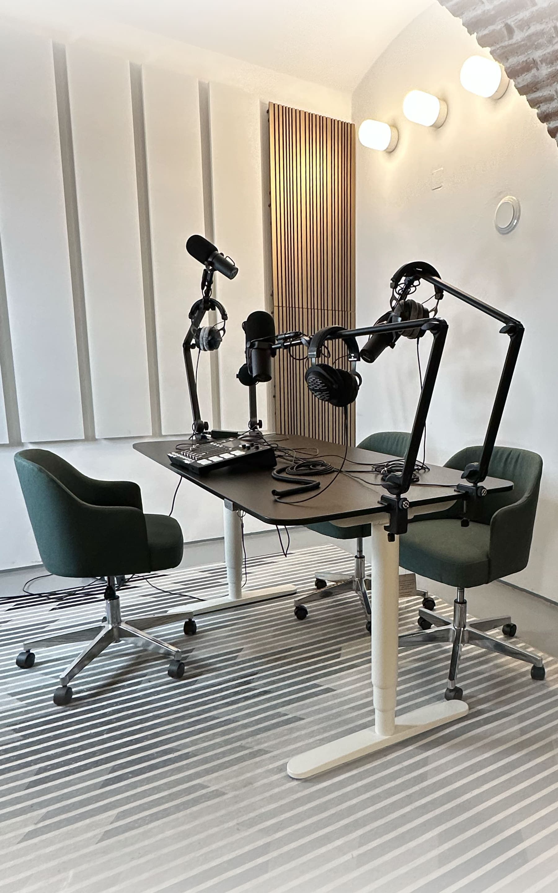 Die Podcast-Ecke: schwarzer Tisch mit drei Mikrofonen an Armen, Kopfhörern und einem Aufnahmegerät, drumherum drei grüne Sessel.