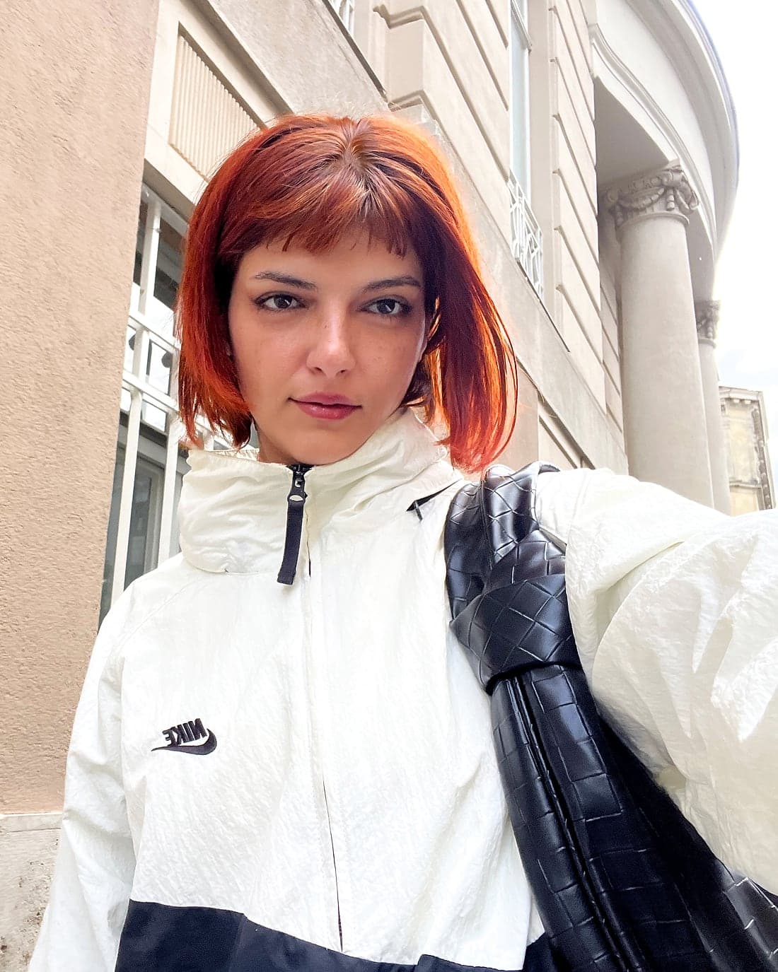 Wered Fuchs mit rotem Haar und weißer Jacke vor einer hellen Hauswand.